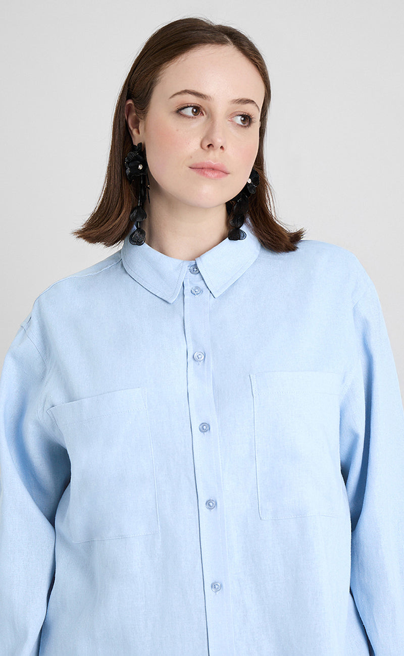 Ein Curvymodel ist vor einem hellen einfarbigen Hintergrund bis zur Taille abgebildet. Sie trägt Curvy Bluse 'Shirin' in hellblau aus der Guido Maria Kretschmer Kollektion.