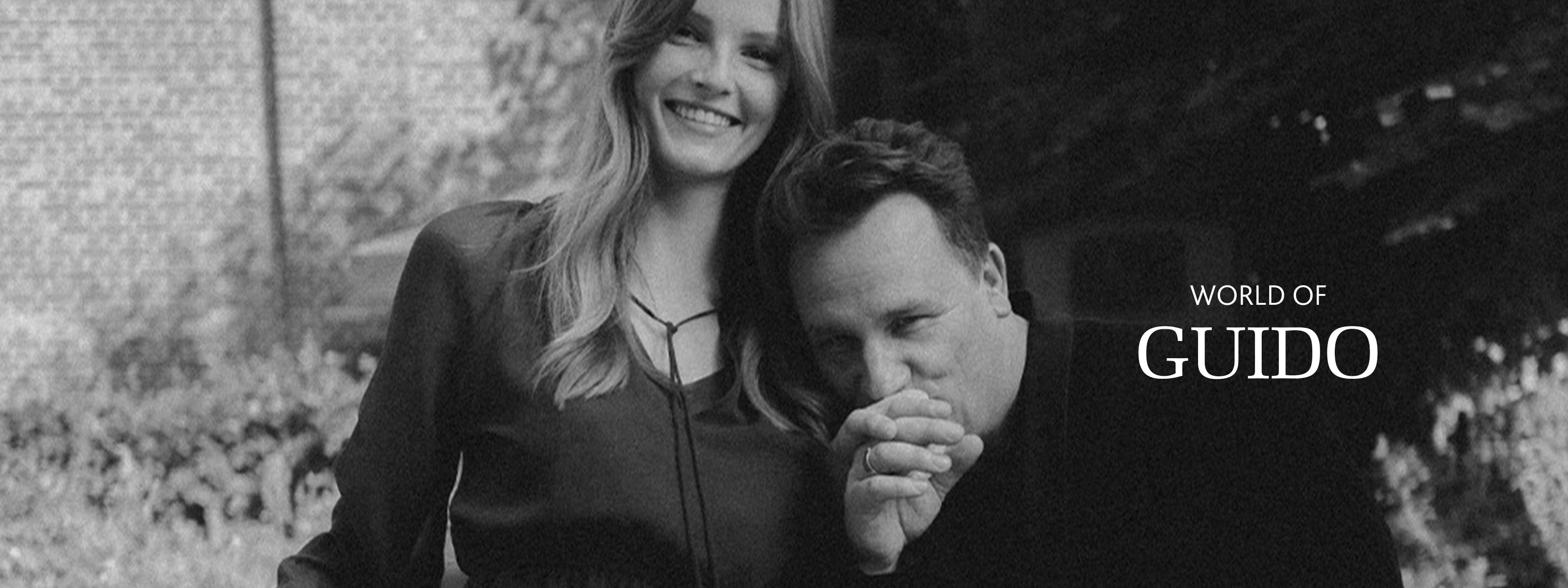 Damenmodel mit Guido Maria Kretschmer in Schwarz-Weiß-Aufnahme. Guido küsst die Hand der Dame. Auf der rechten Seite steht "World of Guido".