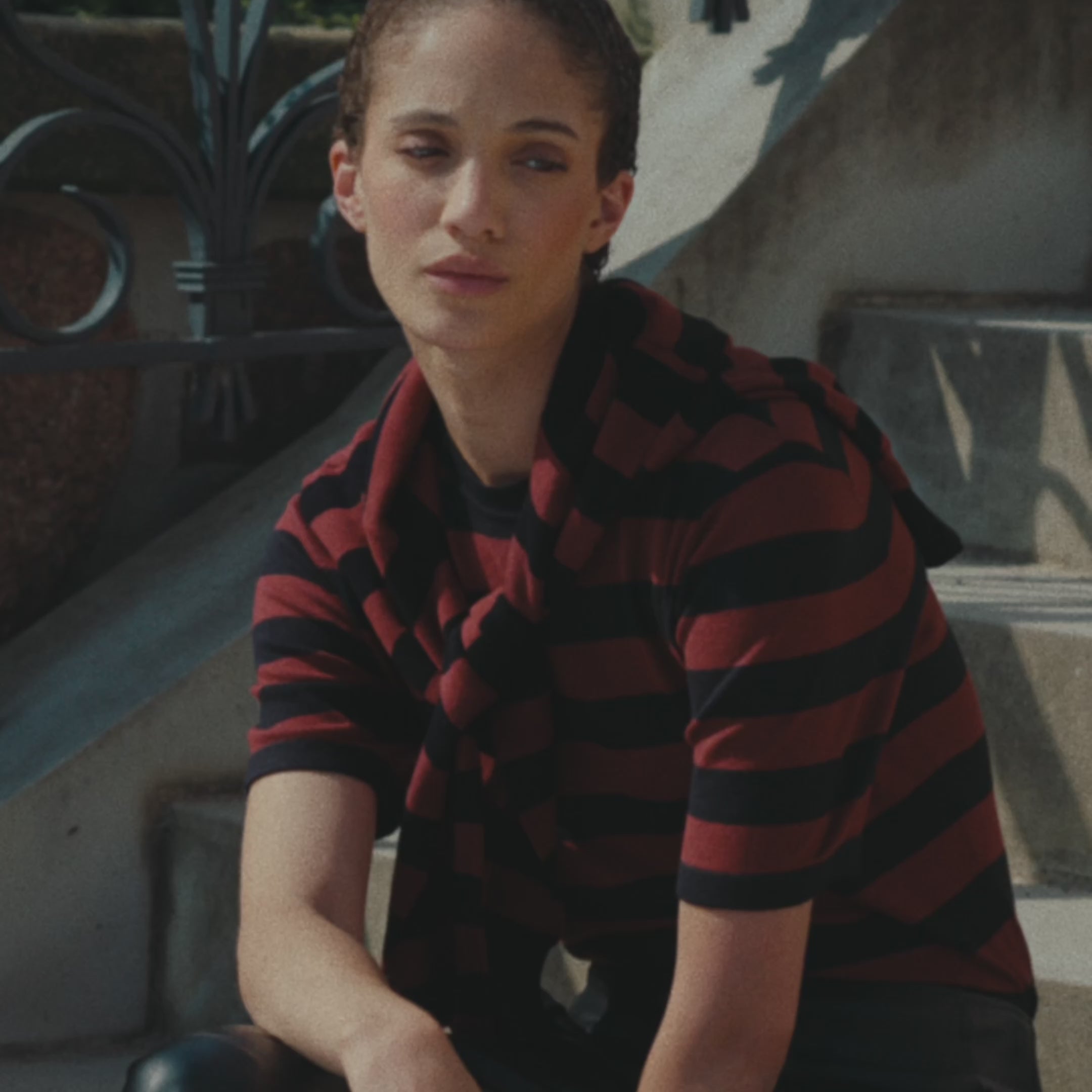 Ein Model sitzt auf der Treppe und wird gefilmt, wie sie dort sitzt mit einem rot-schwarz gestreiften T-Shirt und einer schwarzen Lederhose an.